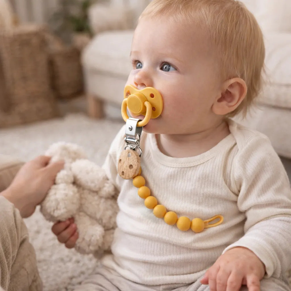Bébé assis sur un tapis à la maison avec une attache tétine silicone jaune et clip en bois