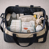Grand sac maternité beige et bleu ouvert montrant l’intérieur organisé avec couches, lingettes, biberon, crème, lange et accessoires bébé soigneusement rangés