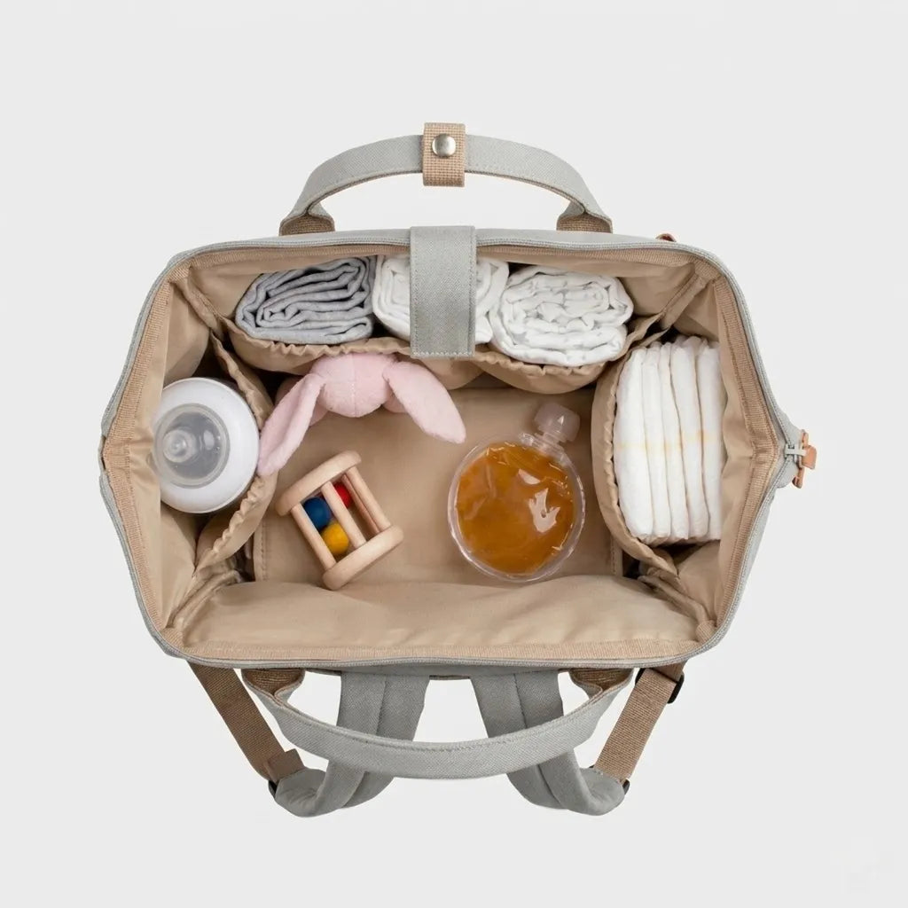 Vue de dessus de l'intérieur d'un sac à dos à langer gris ouvert avec couches, bodies roulés, biberon, hochet et doudou lapin organisés