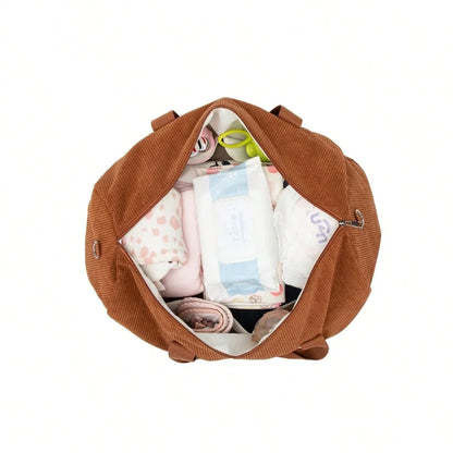 Vue du dessus de l'intérieur du sac à langer caramel en velours côtelé, rempli de vêtements bébé, lingettes, couches et accessoires, illustrant sa grande capacité