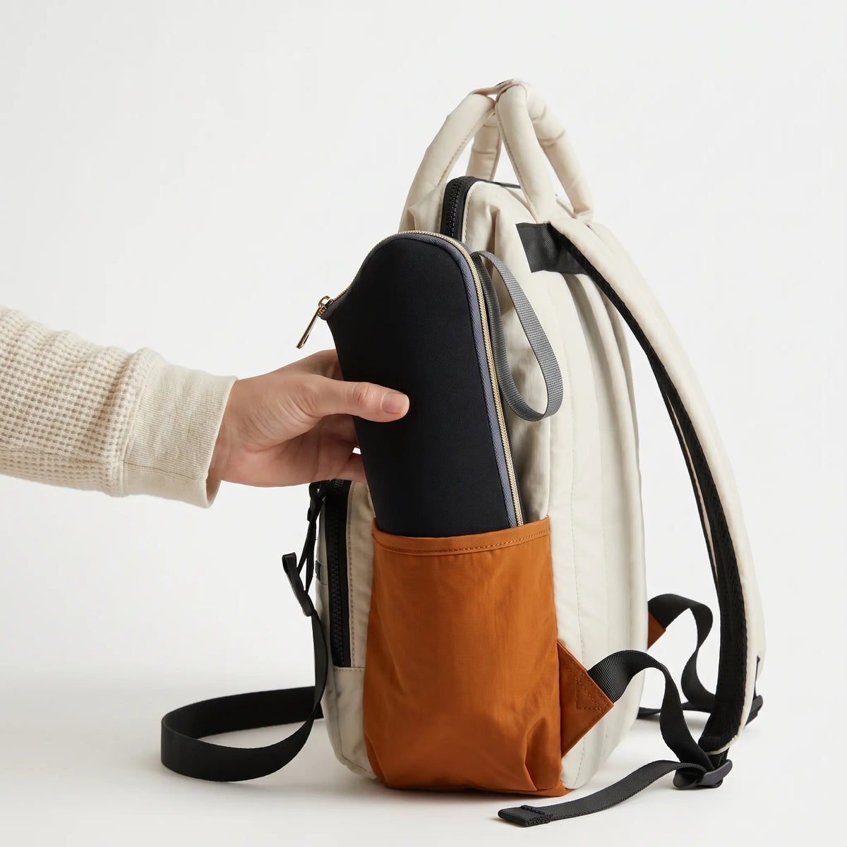 Pochette isotherme biberon noire avec zip doré insérée dans la poche latérale 
orange d'un sac à dos à langer crème bicolore — photo lifestyle studio 
démonstration usage produit