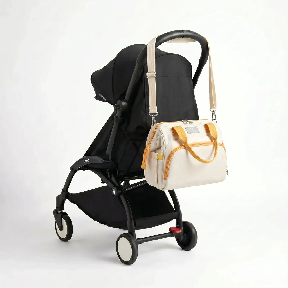 Pochette isotherme bébé bicolore écru avec anses et finitions moutarde et bandoulière accrochée au guidon d'une poussette compacte noire de type Yoyo