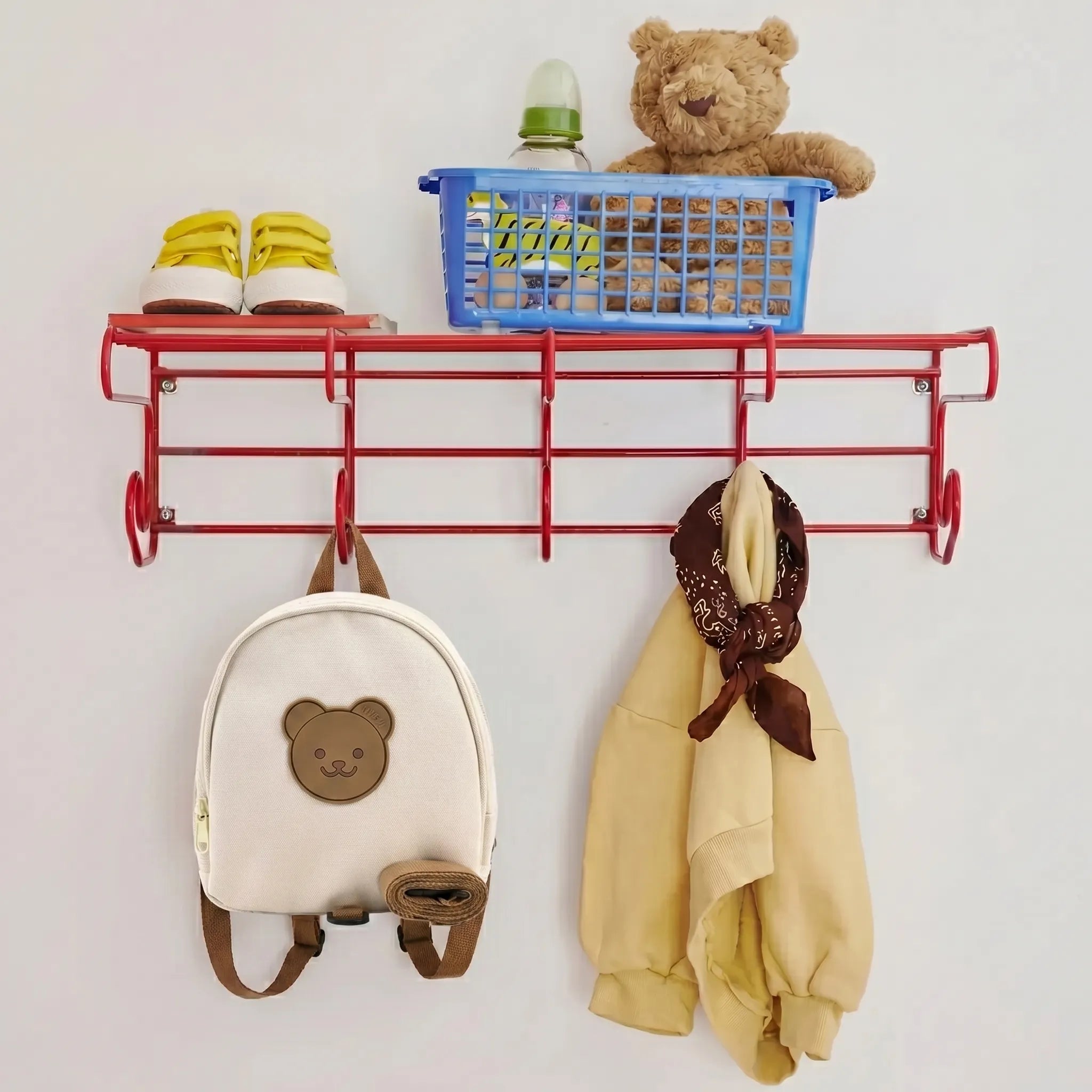 Sac à dos crèche beige en toile canvas avec écusson ourson et sangle de sécurité anti-fugue accroché à un porte-manteau enfant à côté d'un sweat beige, de baskets jaunes et d'un panier avec biberon et doudou