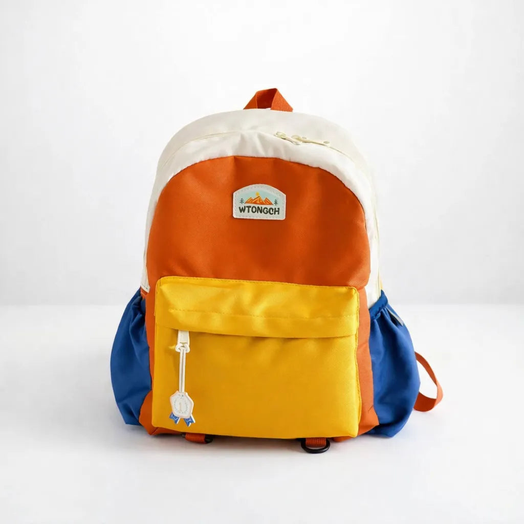 Sac à dos enfant multicolore (orange, jaune, bleu et crème) photographié sur fond blanc en studio, avec poche avant zippée et poches latérales, idéal pour école maternelle et sorties.