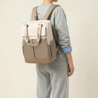 Personne de dos portant un sac à dos à langer bicolore crème et taupe avec bretelles 
ergonomiques maillées et hardware doré — vue lifestyle studio fond blanc chaud