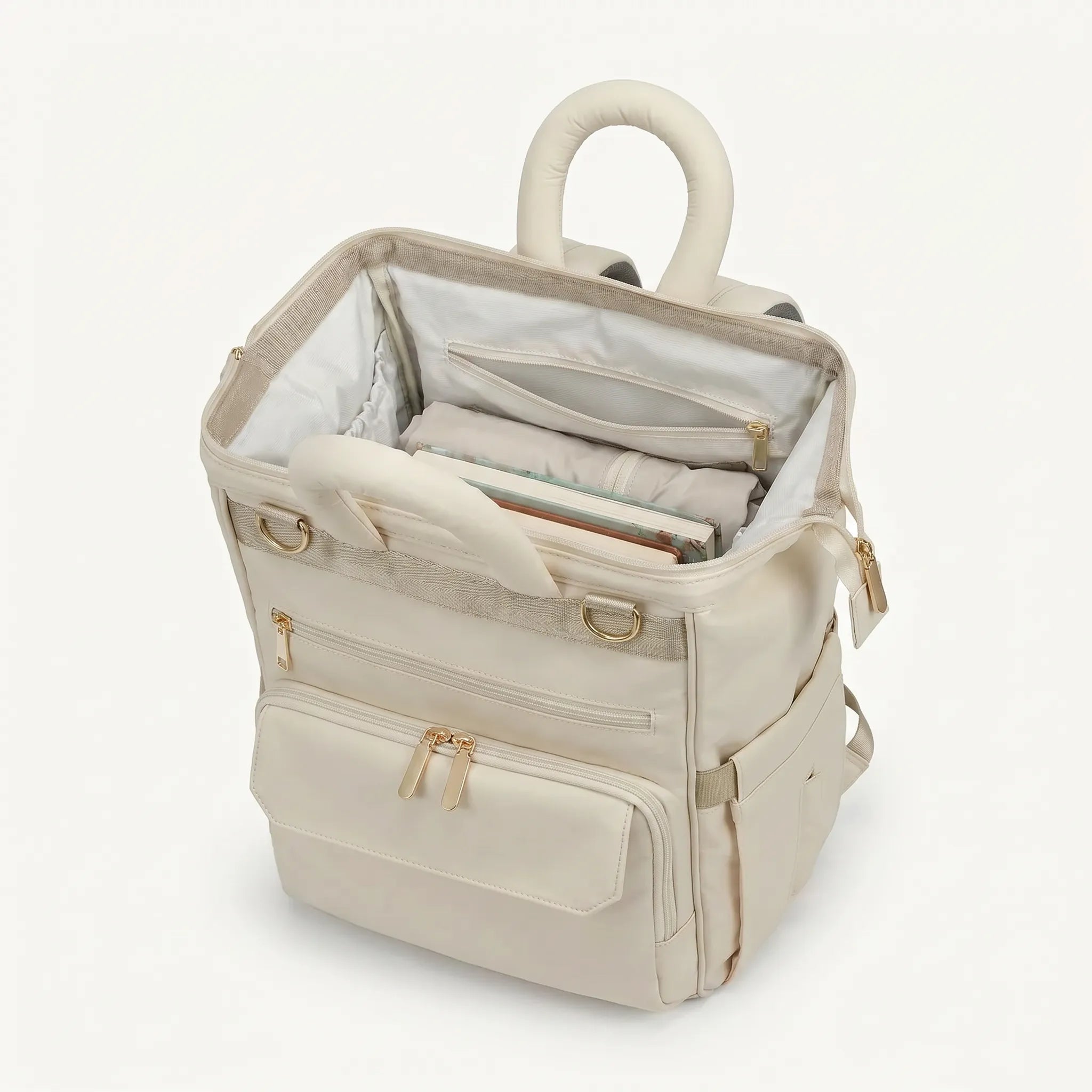 Sac à dos à langer ivoire monochrome vue de dessus, compartiment principal ouvert 
avec doublure blanche, poche zippée intérieure et poignée tubulaire rembourrée 
— compatible valise trolley