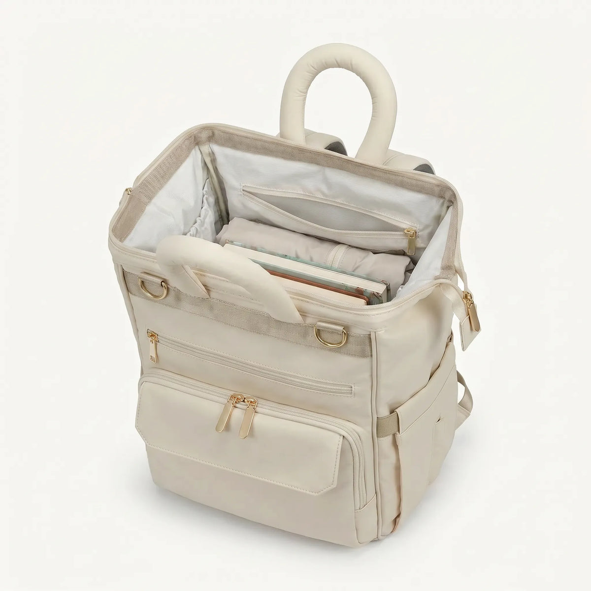 Sac à dos à langer ivoire monochrome vue de dessus, compartiment principal ouvert 
avec doublure blanche, poche zippée intérieure et poignée tubulaire rembourrée 
— compatible valise trolley