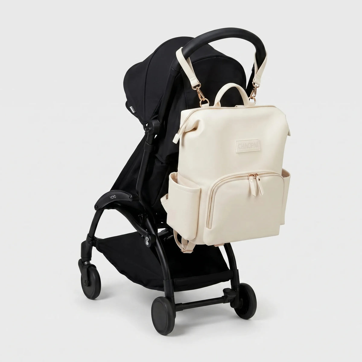 Sac à dos à langer effet cuir écru avec zips dorés et sangles poussette accroché au guidon d'une poussette compacte noire de type Yoyo