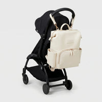 Sac à dos à langer effet cuir écru avec zips dorés et sangles poussette accroché au guidon d'une poussette compacte noire de type Yoyo