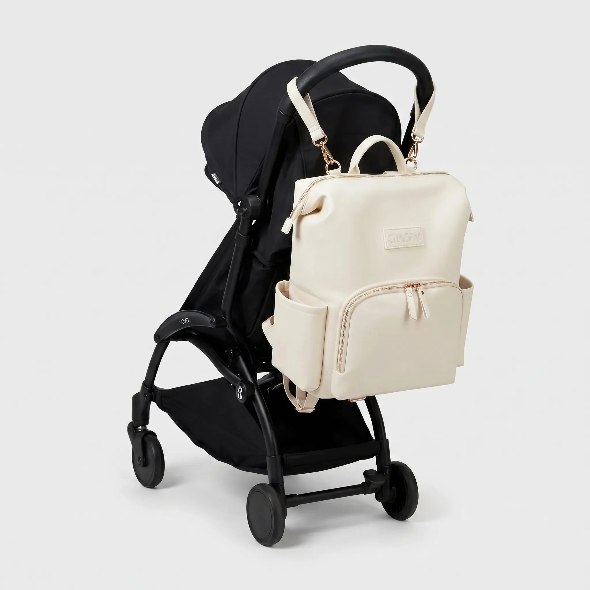 Sac à dos à langer effet cuir écru avec zips dorés et sangles poussette accroché au guidon d'une poussette compacte noire de type Yoyo