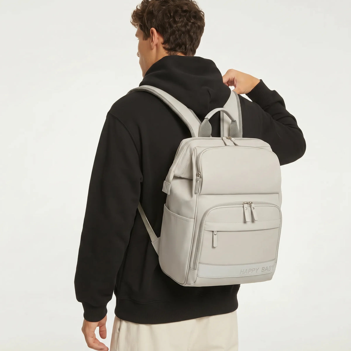 Jeune homme de dos portant un sac à dos à langer gris clair Happy Baby avec bretelles 
ergonomiques maillées, vue lifestyle studio fond blanc