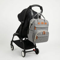 Sac à dos à langer gris chiné avec port USB intégré et accents cuir caramel, 
suspendu au guidon d'une poussette Babyzen YOYO2 noire — vue lifestyle studio