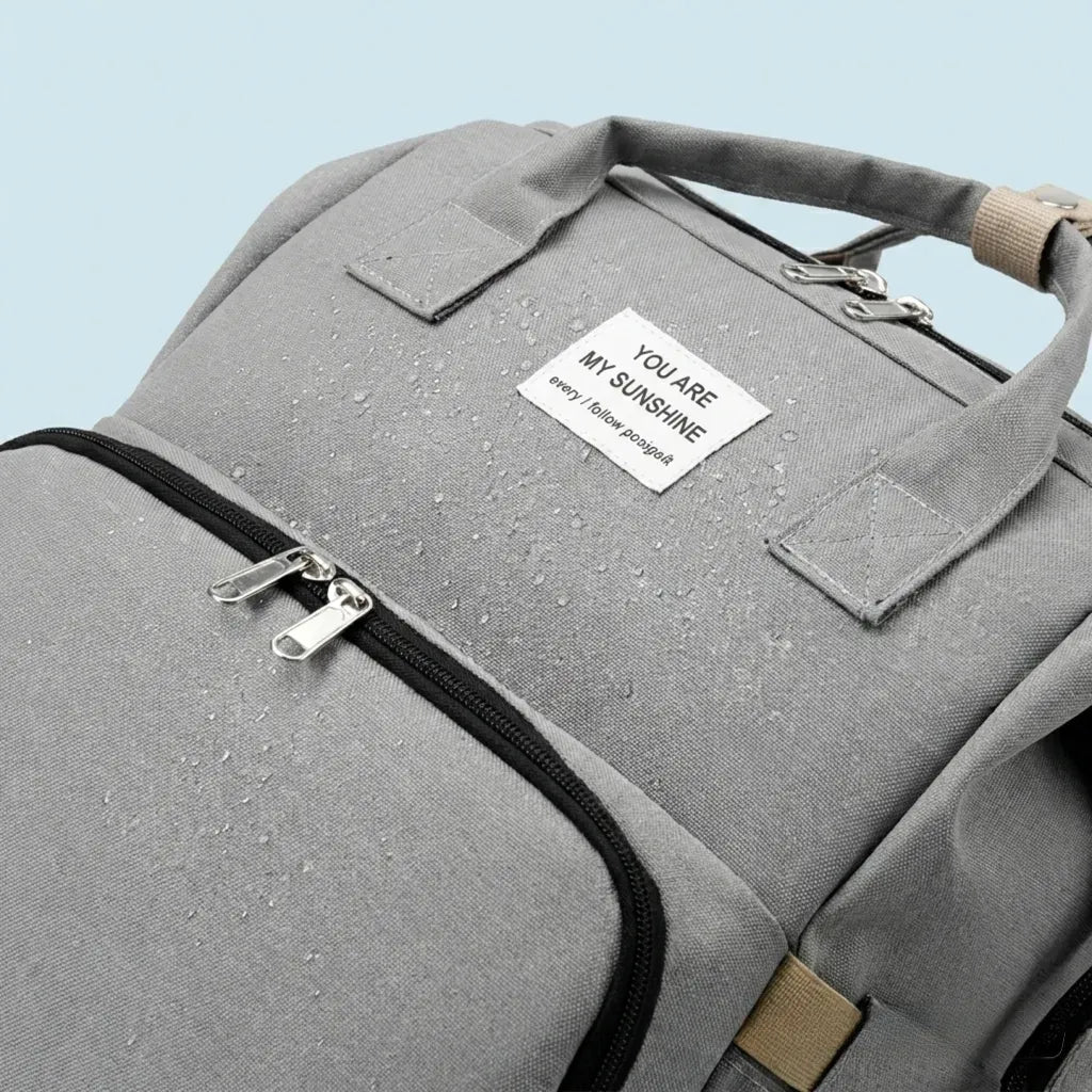 Zoom sur un sac à dos à langer gris avec gouttes d'eau sur le tissu, démontrant son imperméabilité