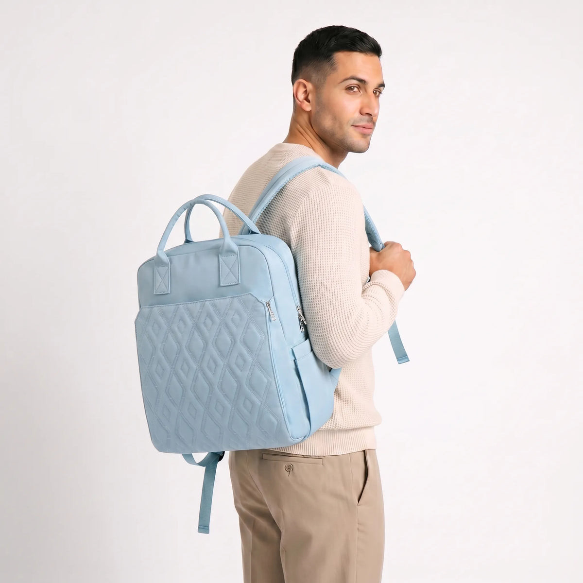Mannequin homme aux cheveux courts en pull waffle crème portant un sac à dos à langer bleu pastel matelassé à motif diamants sur l'épaule droite