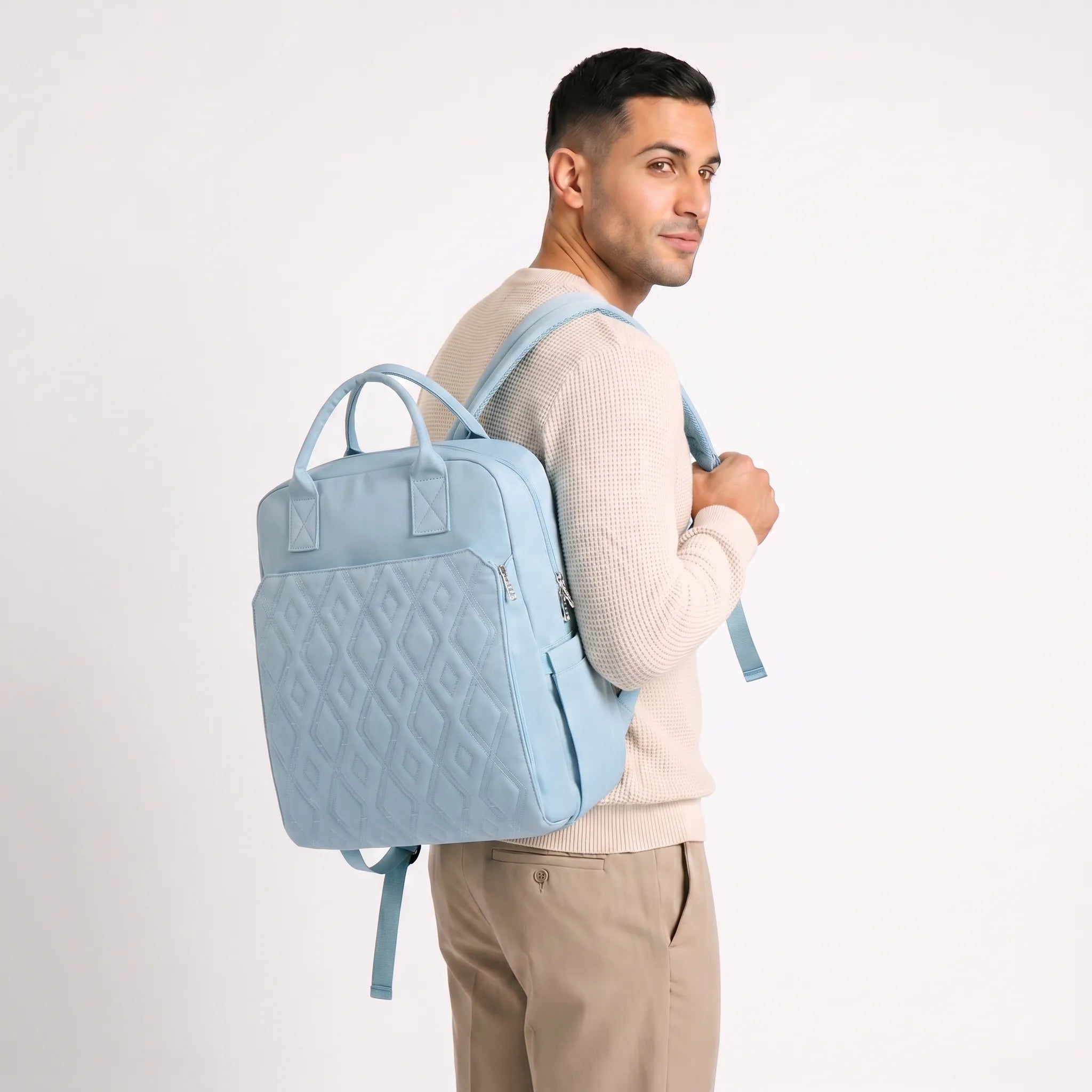 Mannequin homme aux cheveux courts en pull waffle crème portant un sac à dos à langer bleu pastel matelassé à motif diamants sur l'épaule droite
