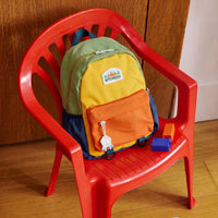 Sac à dos maternelle 2-6 ans au design colorblock vert moutarde orange et bleu posé sur une chaise enfant rouge avec cubes de motricité