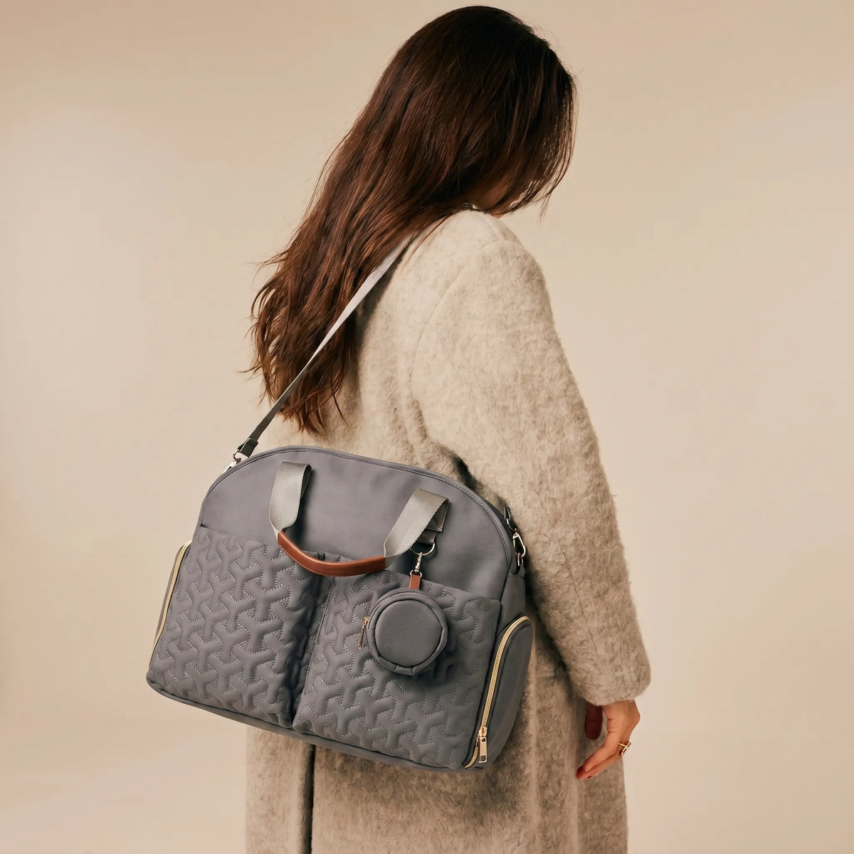 Femme de dos aux cheveux longs portant un sac à langer bandoulière gris matelassé avec pochette tétine sur l'épaule