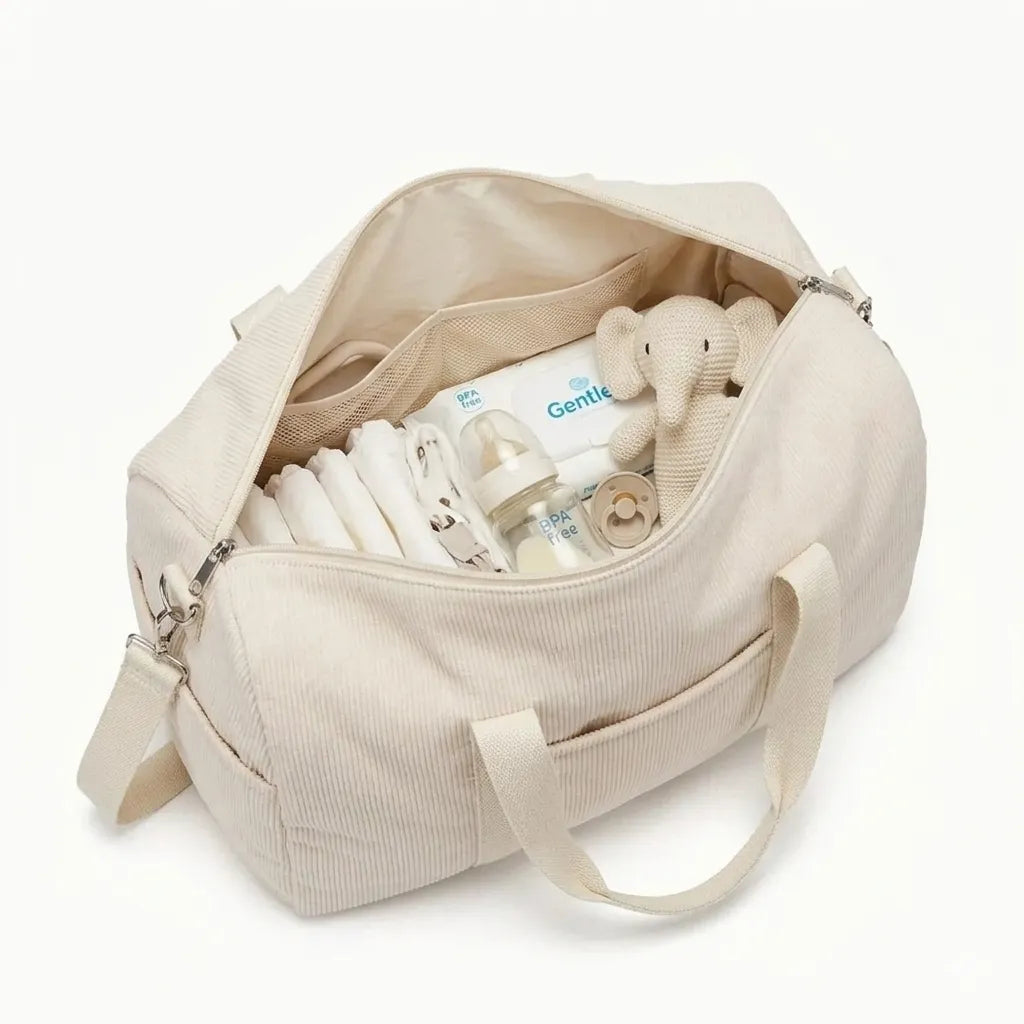 Sac à langer en velours côtelé beige ouvert révélant son contenu : couches, biberon BPA free, sucette, produit de soin Gentle et doudou éléphant tricoté