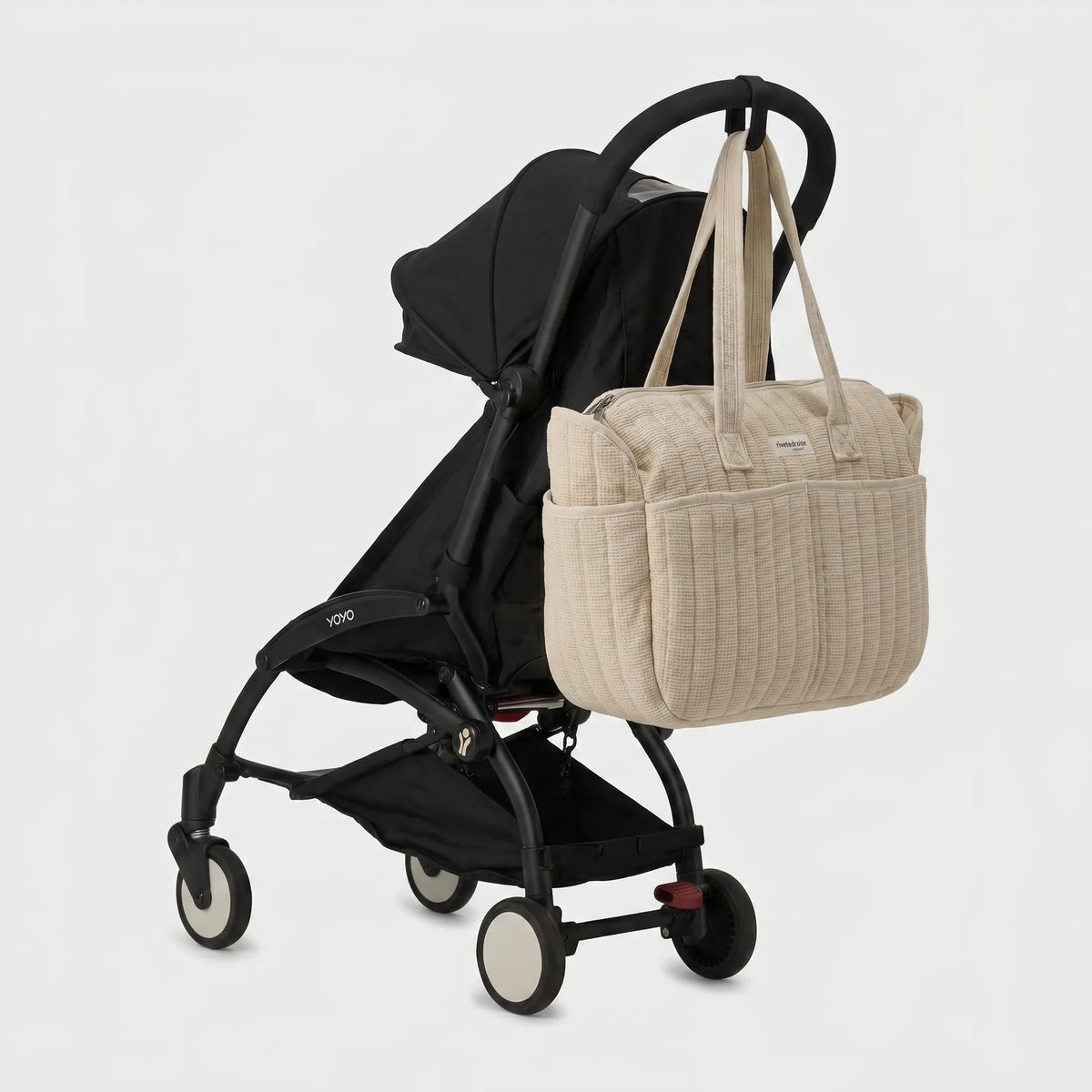 Sac à langer beige matelassé en gaze de coton avec anses longues accroché au guidon d'une poussette compacte noire de type Yoyo