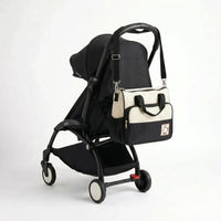 Sac à langer format cabas bicolore écru à pois et noir avec badge ourson et bandoulière accroché au guidon d'une poussette compacte noire de type Yoyo