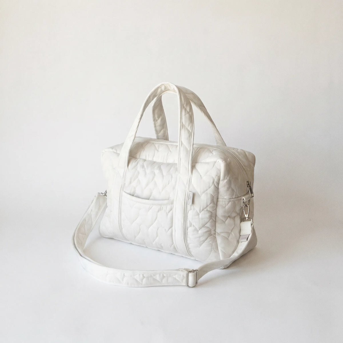 Sac à langer en coton matelassé blanc avec motif diamant, poignées rembourrées 
et bandoulière réglable blanche — packshot studio fond blanc lumière douce