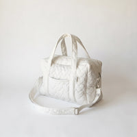 Sac à langer en coton matelassé blanc avec motif diamant, poignées rembourrées 
et bandoulière réglable blanche — packshot studio fond blanc lumière douce
