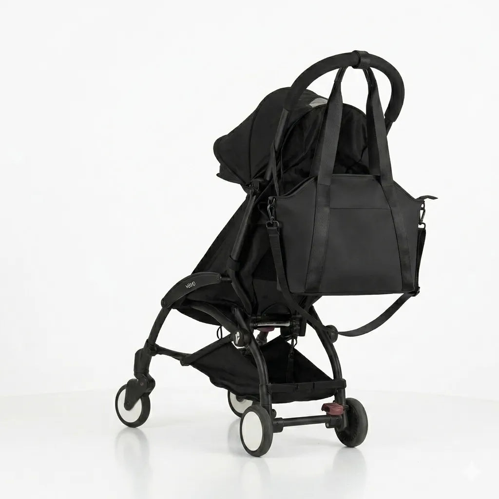 Sac à langer noir bandoulière suspendu à la poignée d'une poussette noire sur fond blanc