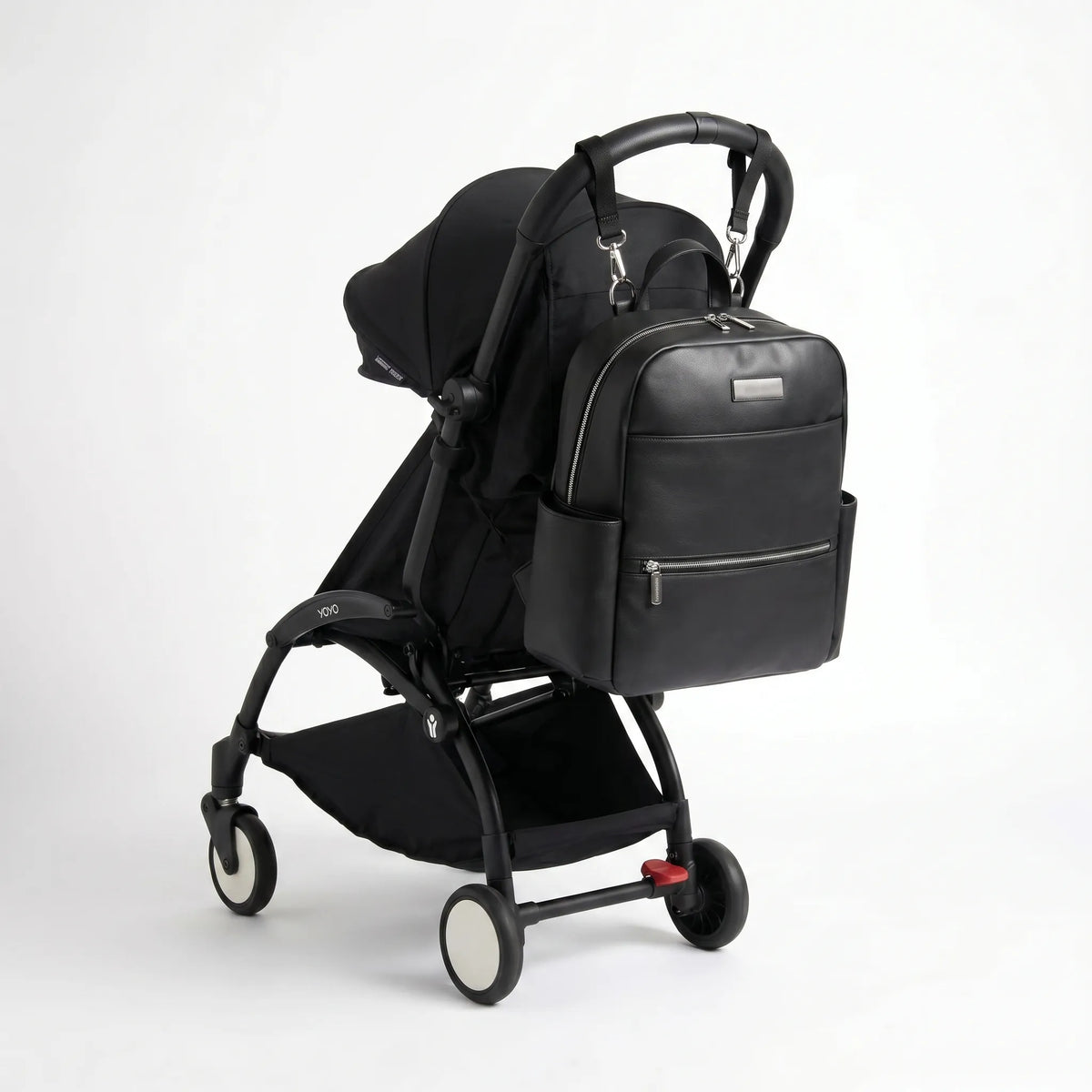 Sac à langer noir en similicuir accroché à une poussette compacte YOYO noire, avec poches zippées et design élégant pour les sorties avec bébé.