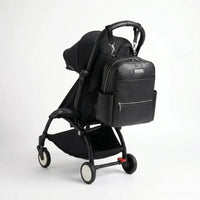 Sac à langer noir en similicuir accroché à une poussette compacte YOYO noire, avec poches zippées et design élégant pour les sorties avec bébé.