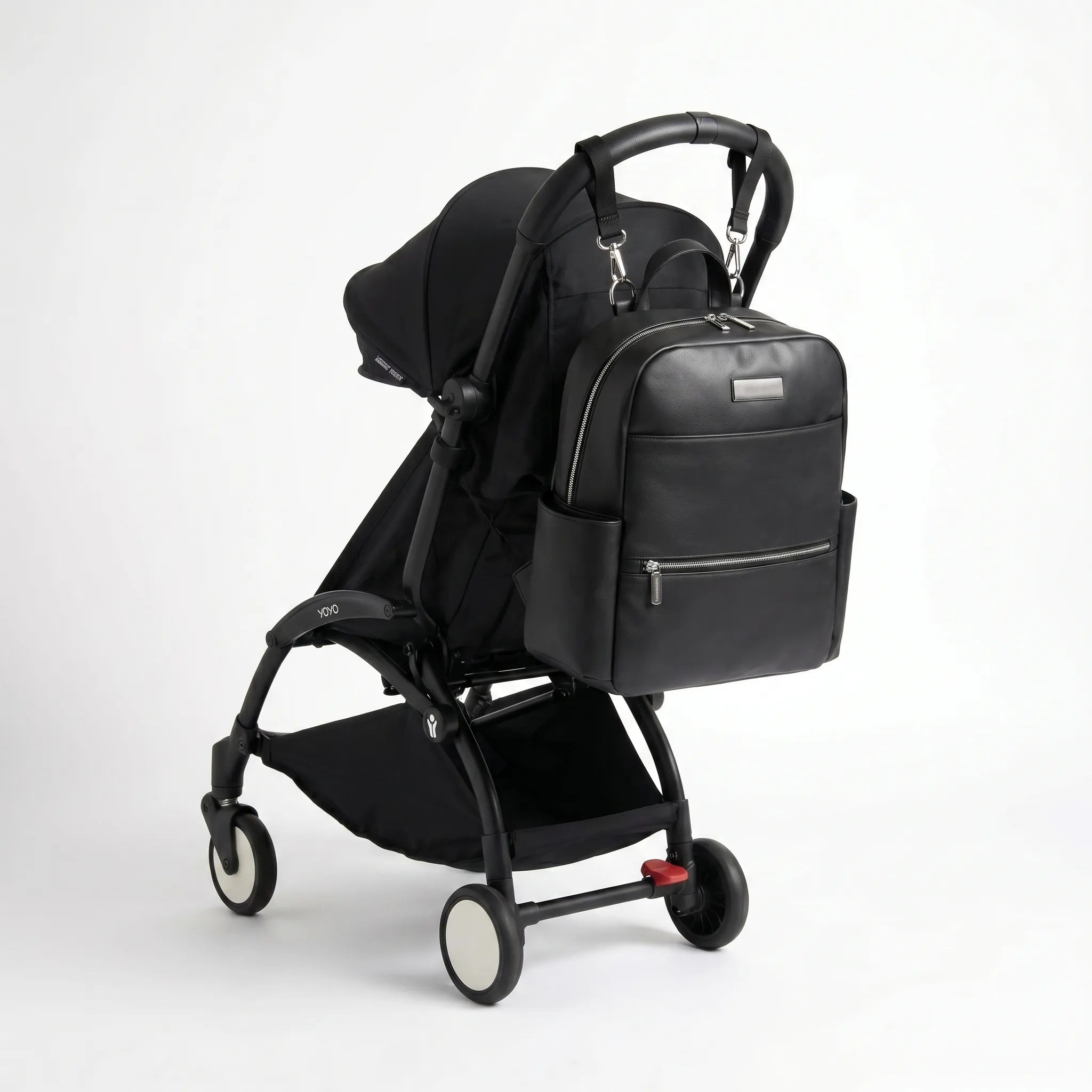 Sac à langer noir en similicuir accroché à une poussette compacte YOYO noire, avec poches zippées et design élégant pour les sorties avec bébé.