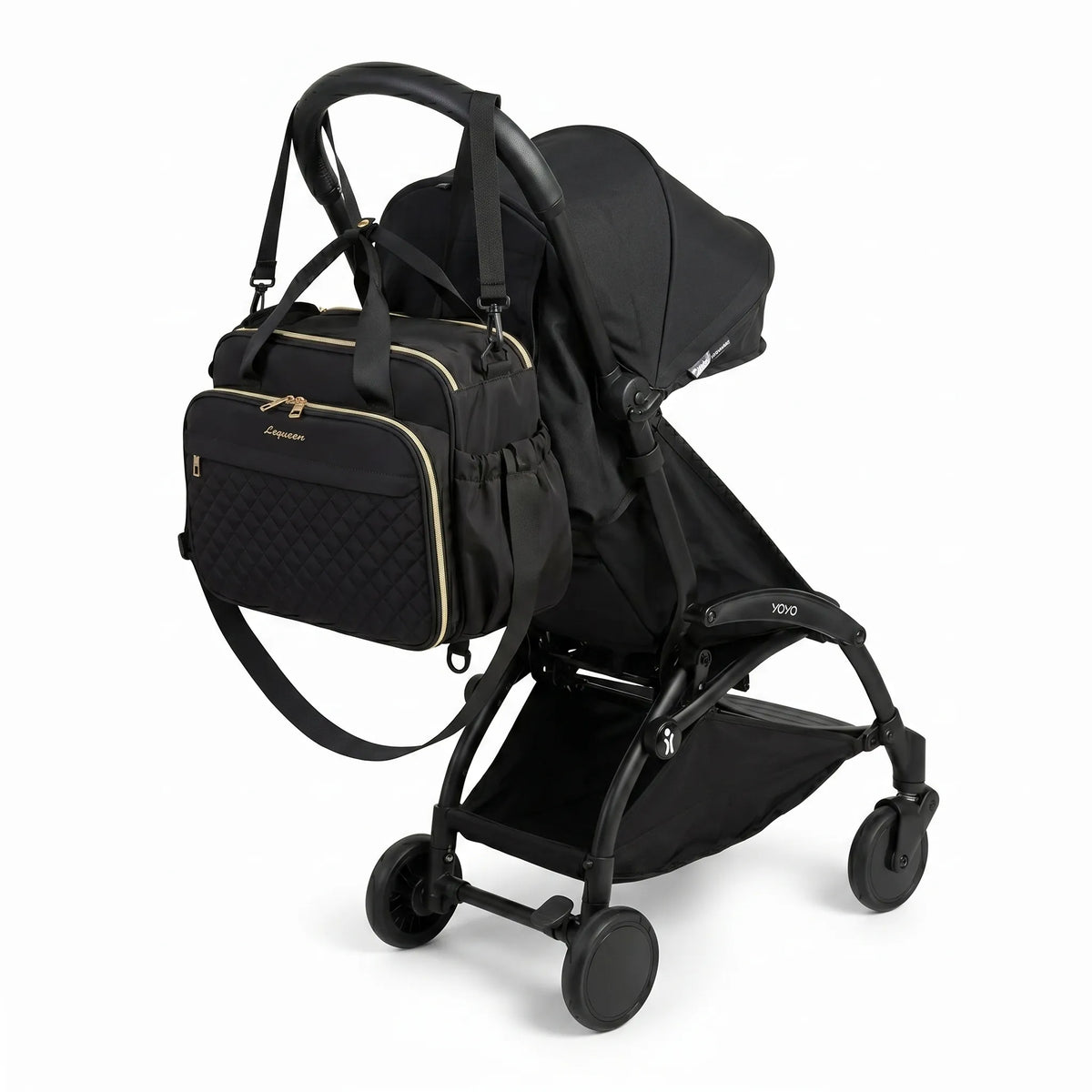 Sac à langer noir matelassé avec zips dorés, bandoulière et poches latérales accroché au guidon d'une poussette compacte noire de type Yoyo