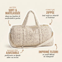 Sac maternité format polochon matelassé beige à imprimé fleuri délicat avec annotations indiquant la matière soft et matelassée douce au toucher, la fermeture zippée sécurisée, la bandoulière ajustable et l'imprimé fleuri intemporel