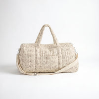 Sac maternité format polochon matelassé beige à imprimé fleuri délicat avec poignées, bandoulière ajustable et poche frontale sur fond clair