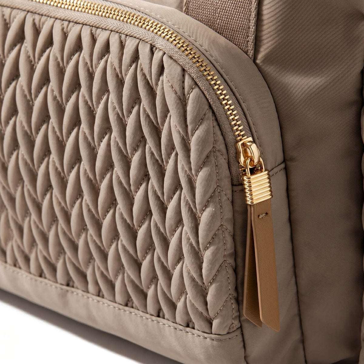 Gros plan sur les détails d'un sac à langer taupe matelassé effet tressé torsadé avec zip doré et tirette en cuir