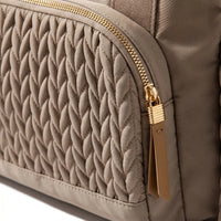 Gros plan sur les détails d'un sac à langer taupe matelassé effet tressé torsadé avec zip doré et tirette en cuir