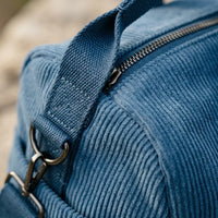 Gros plan sur le tissu velours côtelé bleu d'un sac à langer avec fermeture éclair solide, poignée renforcée et anneau métallique pour bandoulière amovible