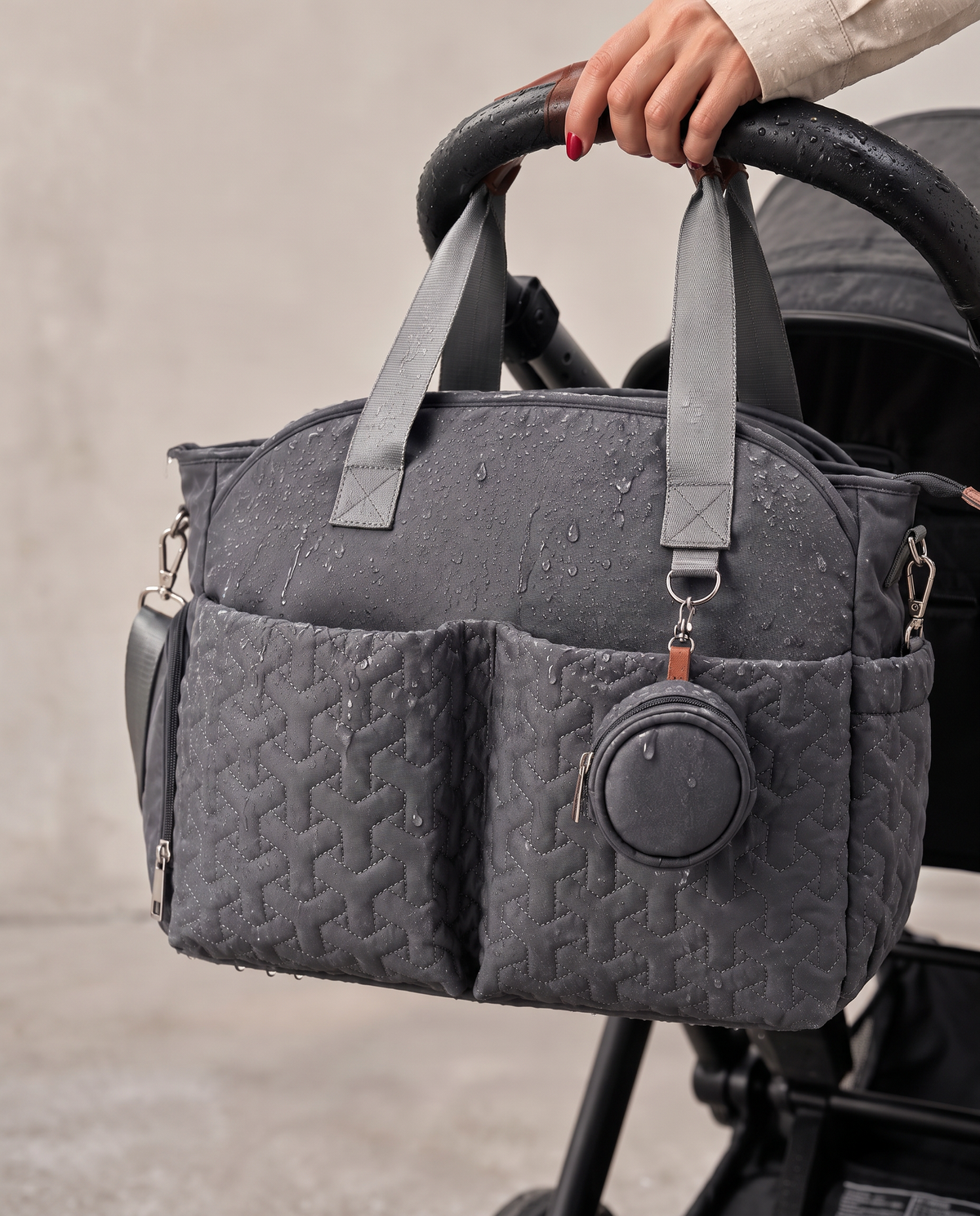 Sac à langer gris matelassé accroché à la poussette sous la pluie