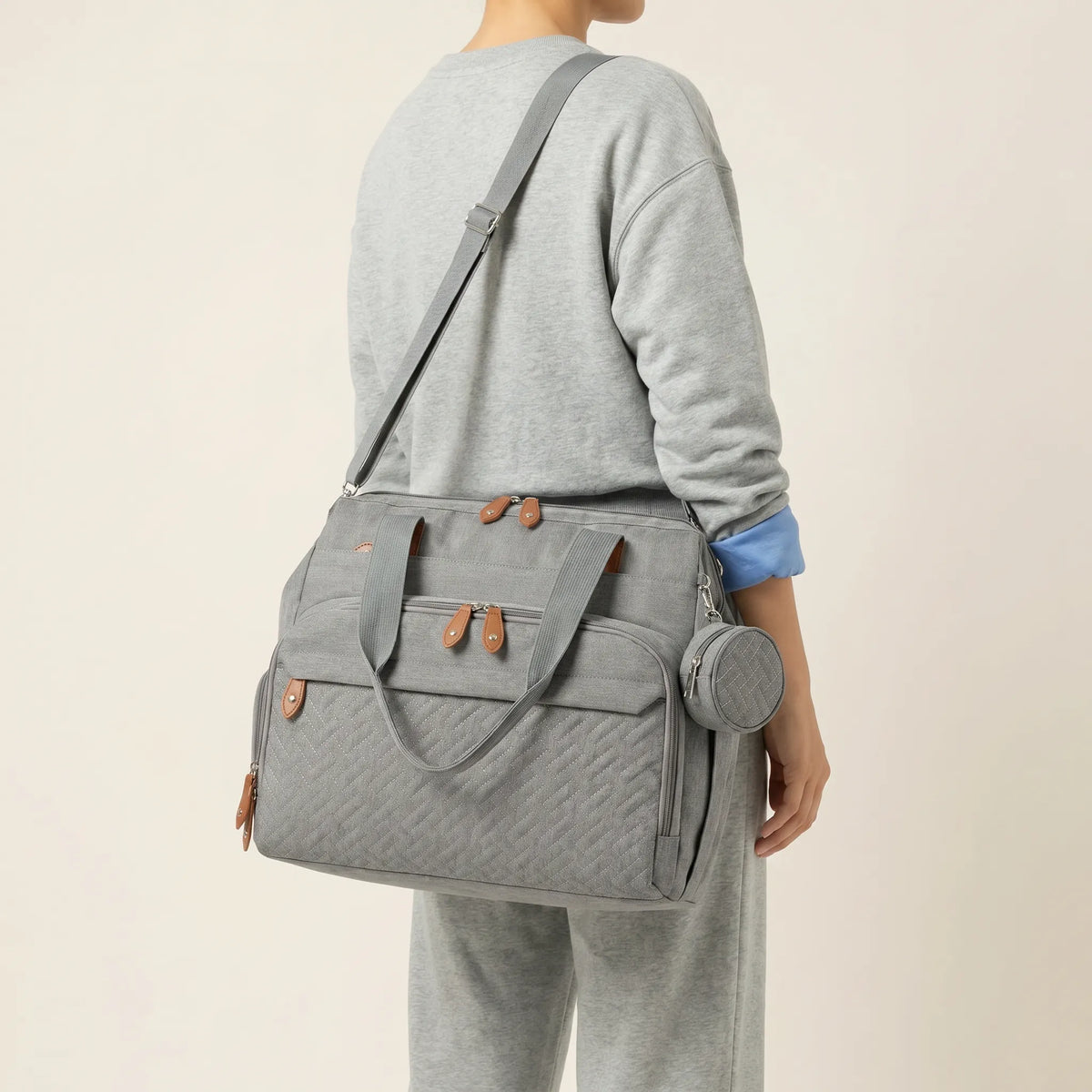 Sac à langer voyage gris porté en bandoulière diagonale vue de dos avec pochette ronde matelassée visible