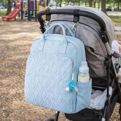 Sac à dos à langer zippé bleu fixé sur poussette au parc – poche biberon accessible et sangles poussette intégrées