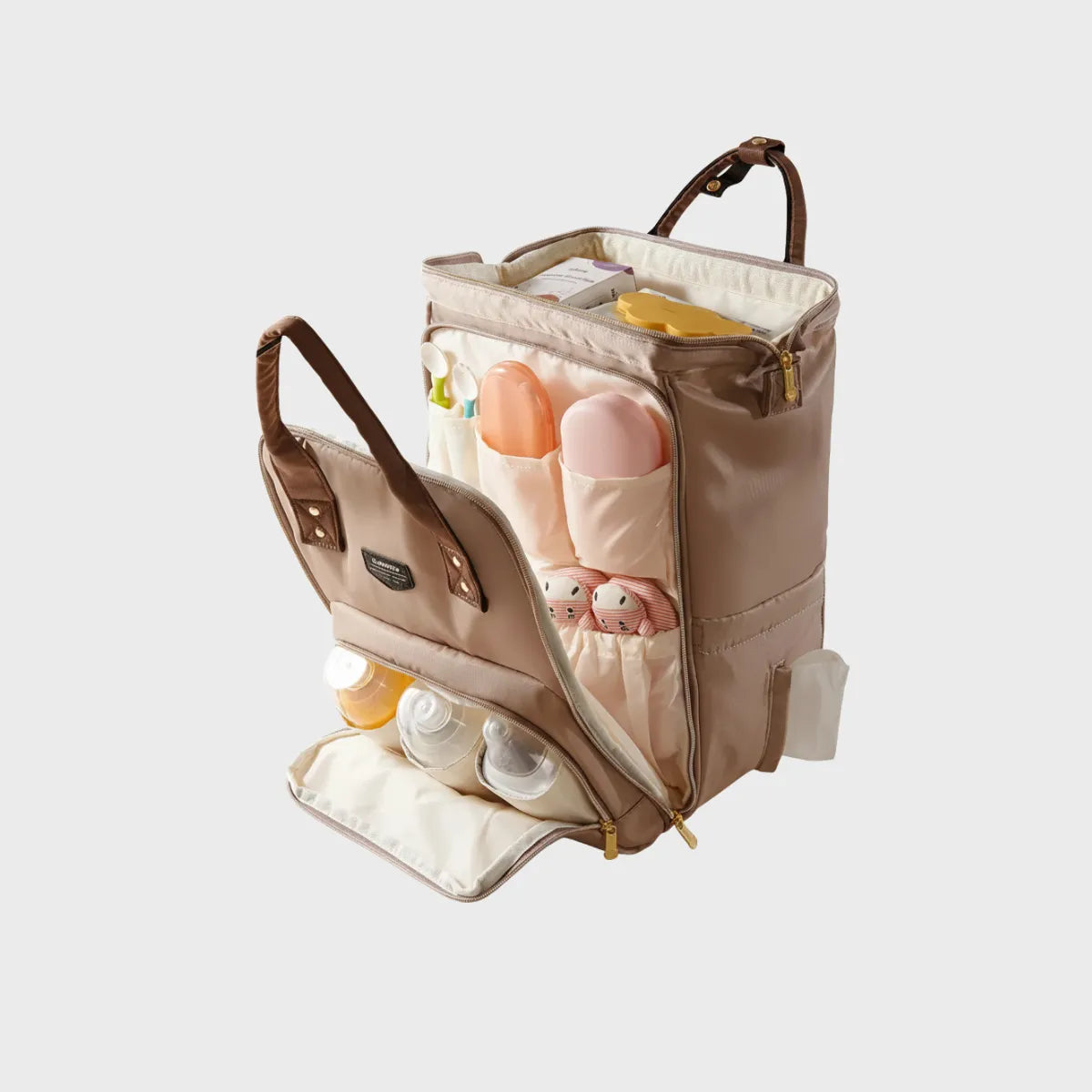 Vue éclatée d'un sac à dos à langer beige ouvert montrant le grand compartiment central, les poches avant pour biberons isothermes, les rangements pour couverts et la fente latérale pour lingettes.
