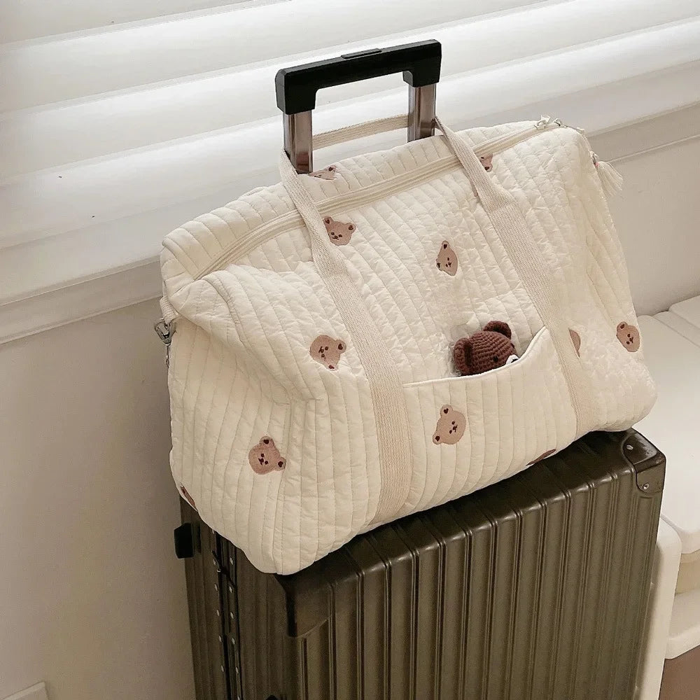 sac à langer en coton matelassé posé sur une valise grâce à la sangle.